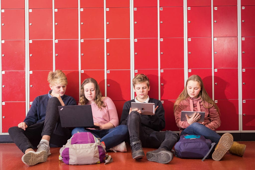 Kinder mit Laptops sitzen vor Schul-Schließfächern