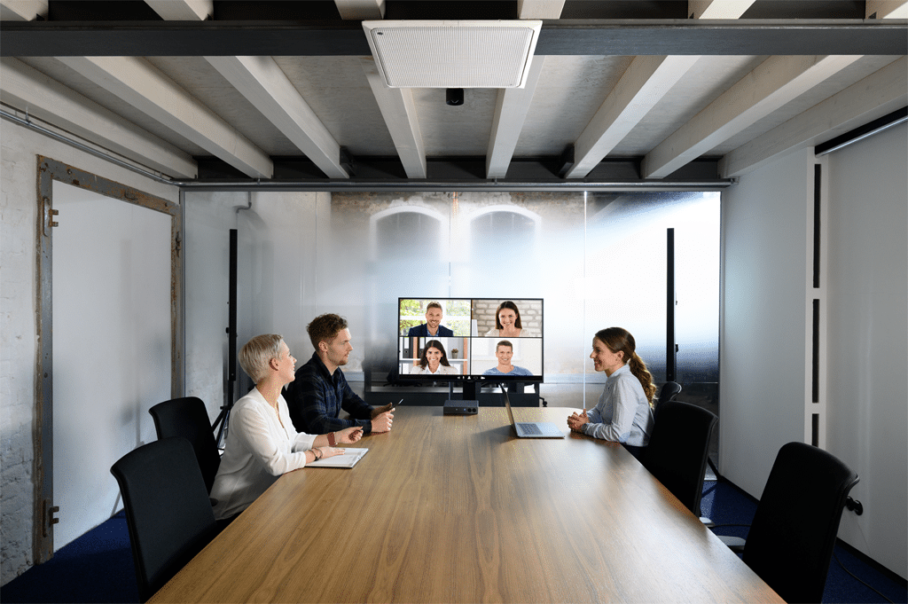 Drei Leute sitzen in einem Meetingraum, per Videokonferenz sind Leute dazugeschaltet
