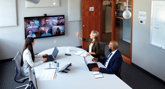 Drei Personen sitzen in einem Meetingraum in einer Videokonferenz