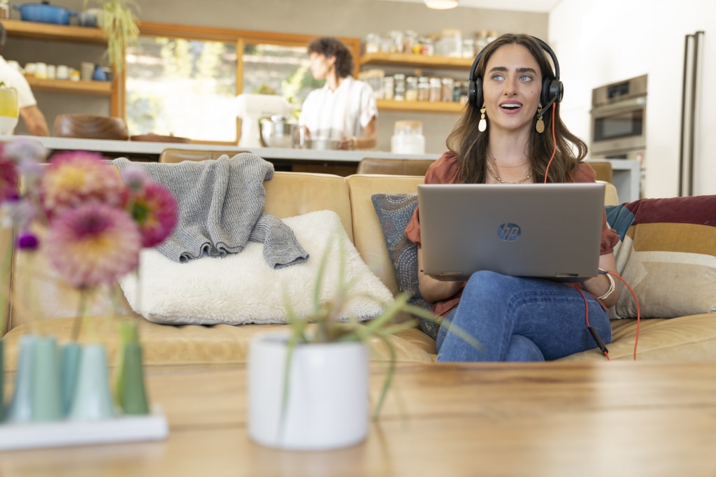 Person mit Kopfhörern und Laptop sitzt auf Sofa