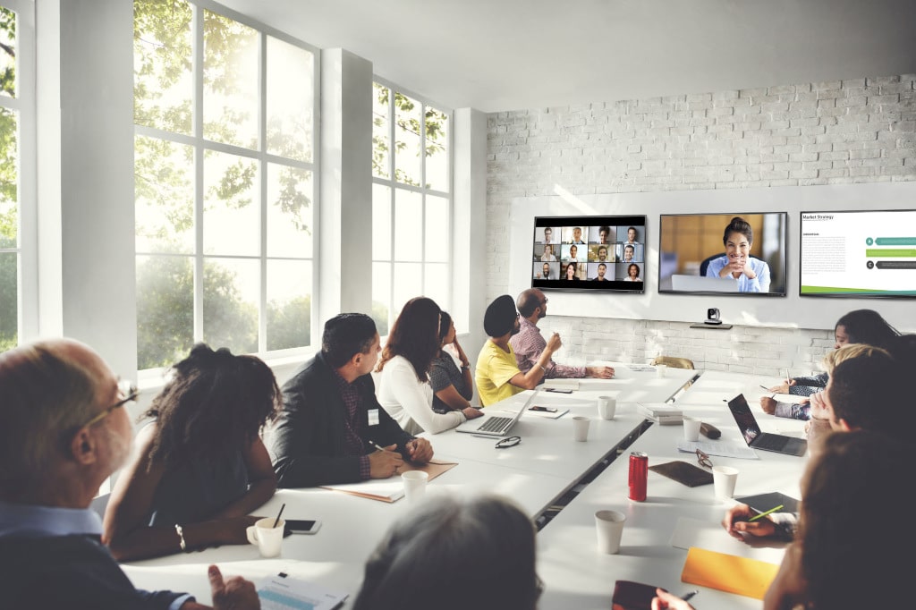 Vollbesetzter Konferenzraum mit Zoom Room in Videokonferenz