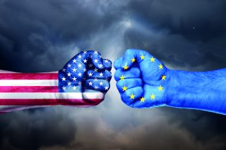 Flags of USA and EU painted on two fists on sky background. United States of America versus EU trade war disputes concept. Sanctions policy.