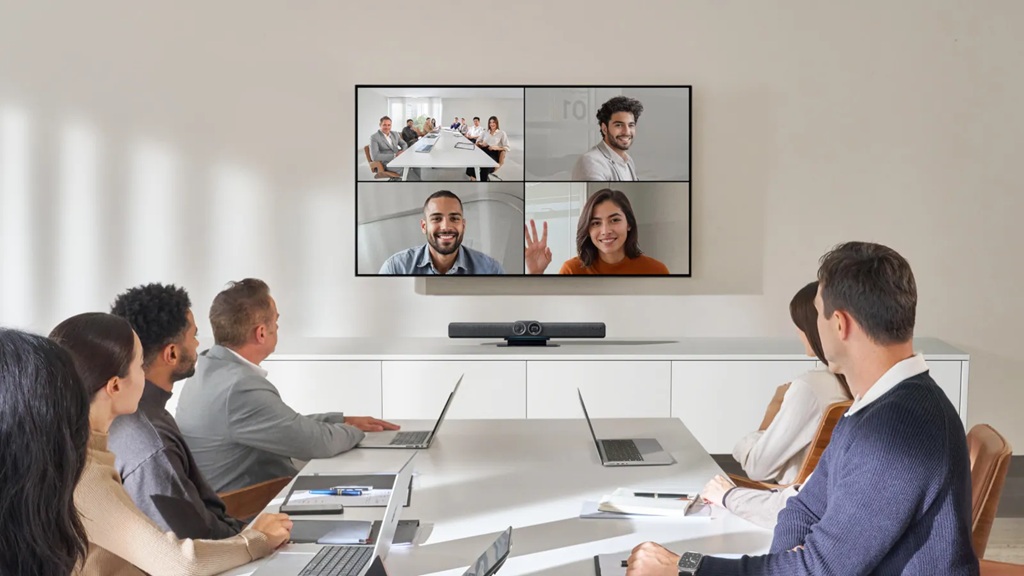 Gruppe von Menschen an Besprechungstische vor großem Monitor an der Wand