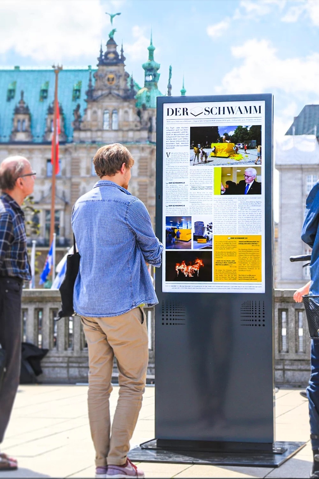 Zwei Männer vor eine Informations-Stele vor einem alten Gebäude