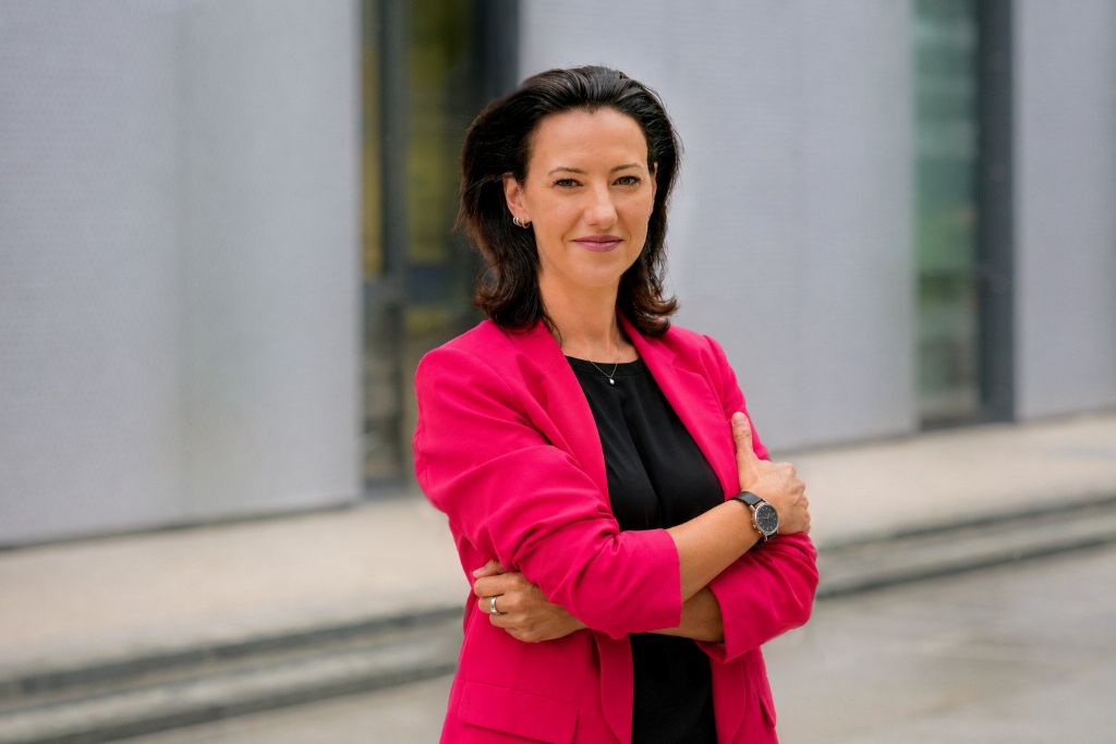 Claudia Feiner im pinkfarbenen Blazer vor einem modernen Gebäude
