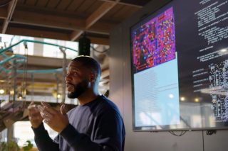 Mann vor großformatigen Displays mit Programmcode und technischen Darstellungen.