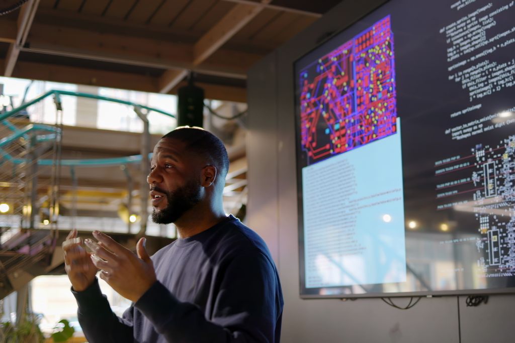 Mann vor großformatigen Displays mit Programmcode und technischen Darstellungen.
