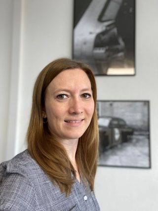 Jenny Köhler steht vor zwei großen Fotografien an einer Wand. Sie blickt frontal in die Kamera