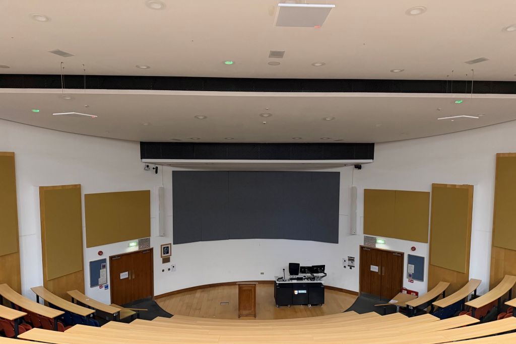 Blick von den ansteigenden, gebogenen Sitzreihen in einen Hörsaal der University of Birmingham mit Rednerpult, AV-Technik und großflächigen Akustikelementen an der Stirnwand.