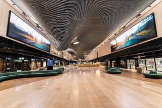 Weitläufiger Terminalbereich des Flughafens Frankfurt mit großformatigen digitalen Displays an beiden Seiten und einer geschwungenen Lamellendecke.