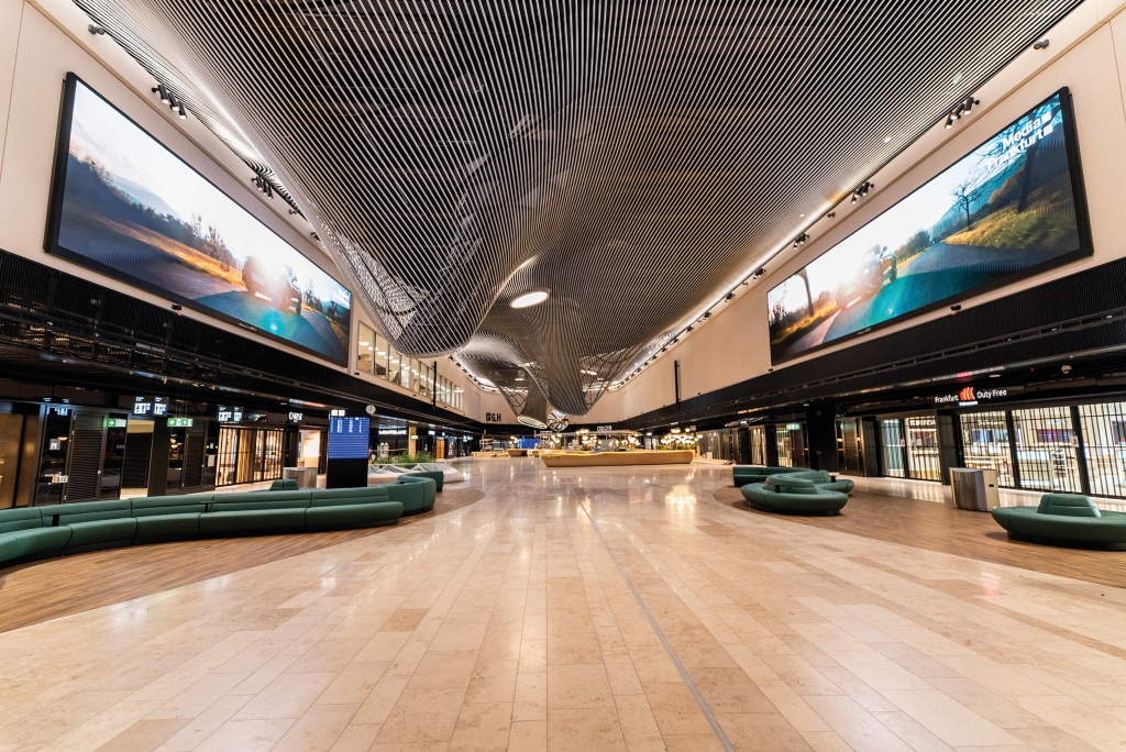 Weitläufiger Terminalbereich des Flughafens Frankfurt mit großformatigen digitalen Displays an beiden Seiten und einer geschwungenen Lamellendecke.