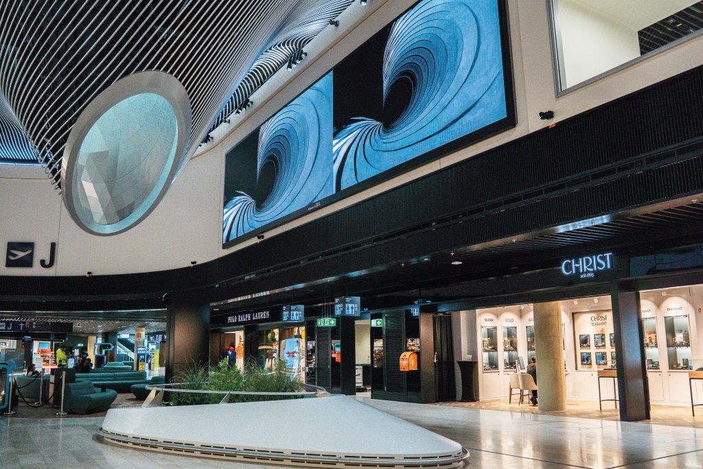 Zwei großformatige digitale Displays mit abstrakten blauen Motiven oberhalb der Geschäfte im Terminal des Flughafens Frankfurt.